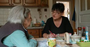 Woman caregiver helping older adult woman at a table.
